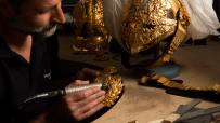 Thomas Lyte designer polishing intricate gold ceremonial helmet detail with a rotary tool.