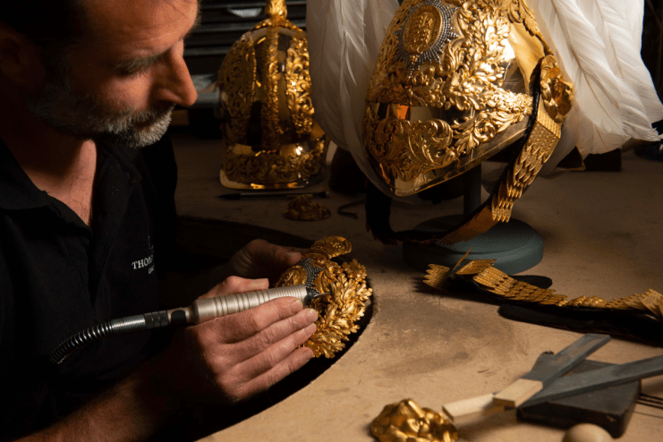 Thomas Lyte designer polishing intricate gold ceremonial helmet detail with a rotary tool.