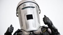 Count Binface in his distinctive silver bin helmet and black armored suit, giving two thumbs up.