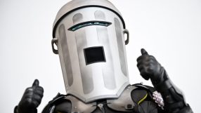 Count Binface in his distinctive silver bin helmet and black armored suit, giving two thumbs up.