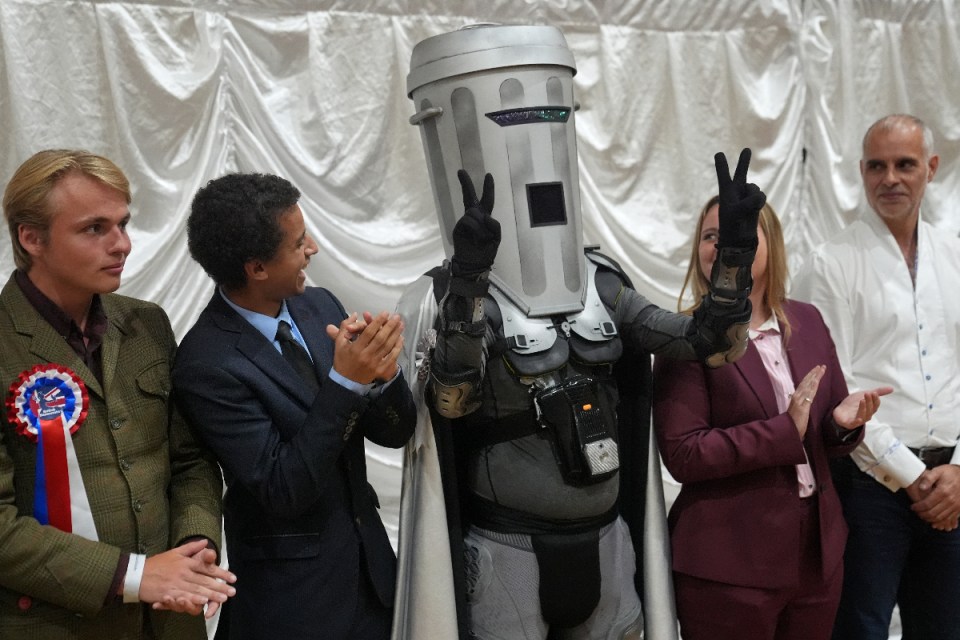 Count Binface, a political candidate in a dustbin-themed costume, makes a peace sign at an event.