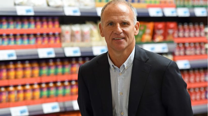Dave Lewis, former Tesco CEO, smiling in a supermarket aisle with products on shelves