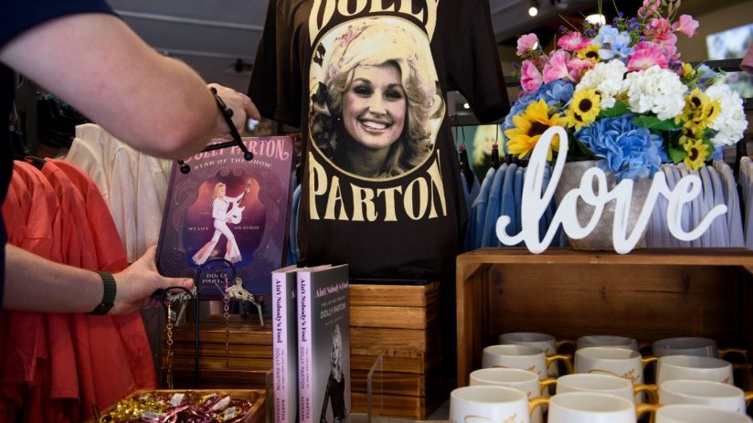 Dollywood gift shop with Dolly Parton t-shirt, books, mugs, and colorful floral display. A person browses merchandise.