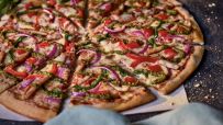 Dominos chicken pesto pizza, sliced, with red onion, bell peppers, and melted cheese on a dark background.