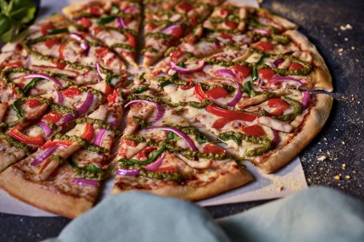 Dominos chicken pesto pizza, sliced, with red onion, bell peppers, and melted cheese on a dark background.