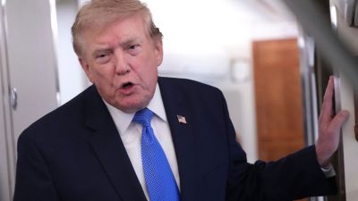 Donald Trump, wearing a blue suit and tie, speaking with his hand resting on a surface indoors.
