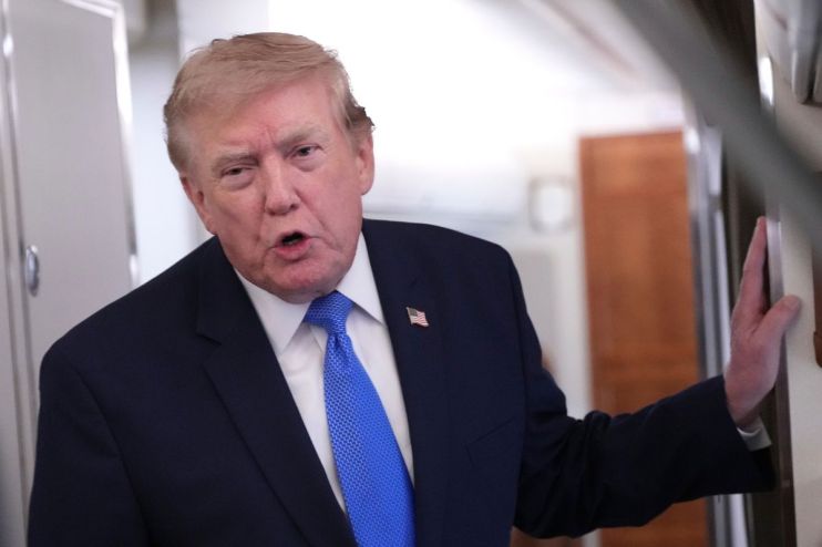 Donald Trump, wearing a blue suit and tie, speaking with his hand resting on a surface indoors.