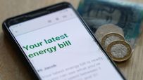 Smartphone displaying an energy bill notification with British coins and a banknote nearby.