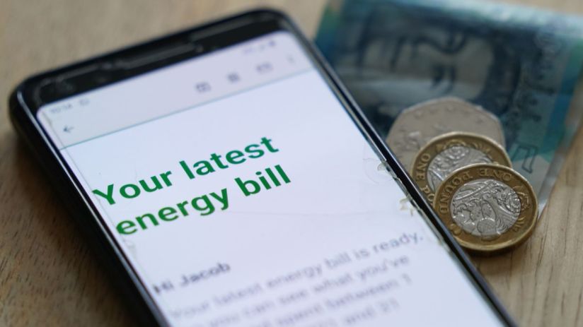 Smartphone displaying an energy bill notification with British coins and a banknote nearby.