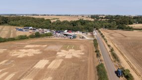 Aerial view of dry, brown farm fields affected by high temperatures, with a road and farm buildings.