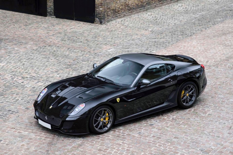 Black Ferrari 599 GTO sports car with yellow brake calipers parked on a cobblestone surface.