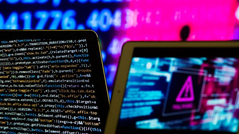 Two tablets displaying code and a cyber warning symbol, with blurry blue and pink background numbers