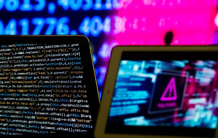 Two tablets displaying code and a cyber warning symbol, with blurry blue and pink background numbers