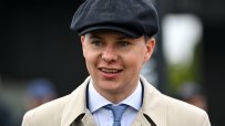 Smiling man in a flat cap and trench coat, light blue tie, white shirt, looking slightly right