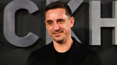 Gary Neville, former footballer and businessman, smiling in a black suit against a dark background