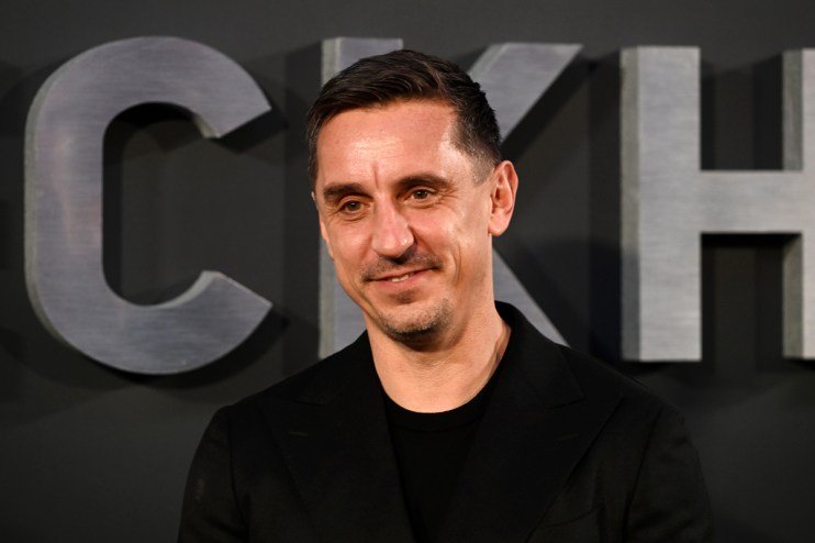 Gary Neville, former footballer and businessman, smiling in a black suit against a dark background
