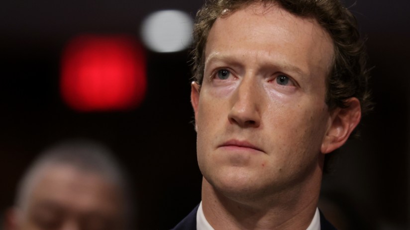 Mark Zuckerberg in a dark suit, looking intently with a red light blurred in the background