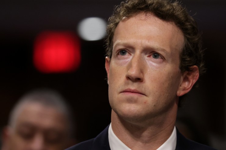 Mark Zuckerberg in a dark suit, looking intently with a red light blurred in the background