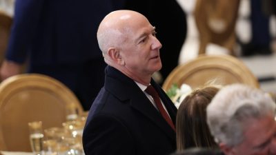 Jeff Bezos, Amazon founder, in a dark suit and red tie at a formal event, looking right.