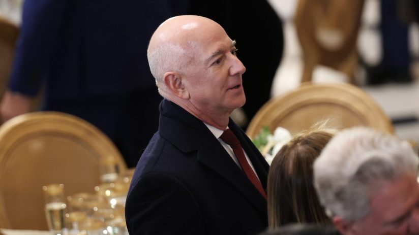Jeff Bezos, Amazon founder, in a dark suit and red tie at a formal event, looking right.