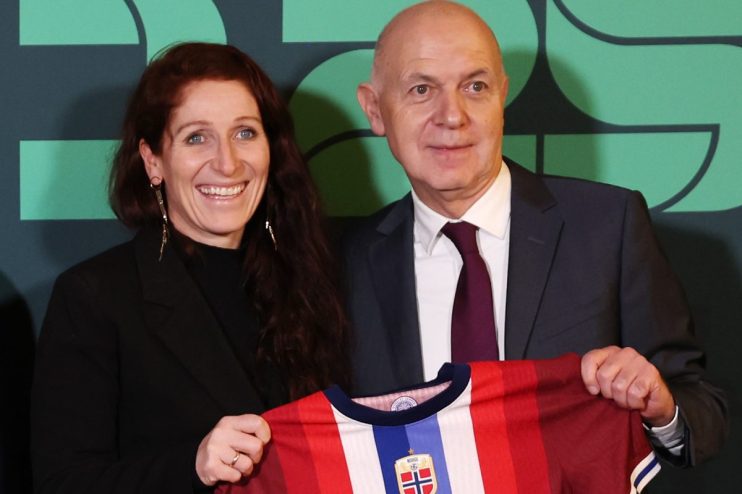 A smiling woman and a man in a suit holding a red, white, and blue soccer jersey with the Norway emblem.