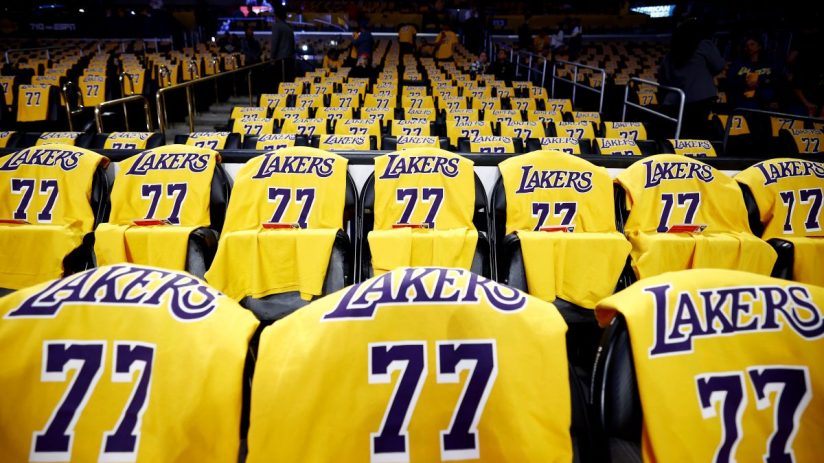 Rows of yellow Lakers jerseys with 77 on seats in a dark basketball arena.