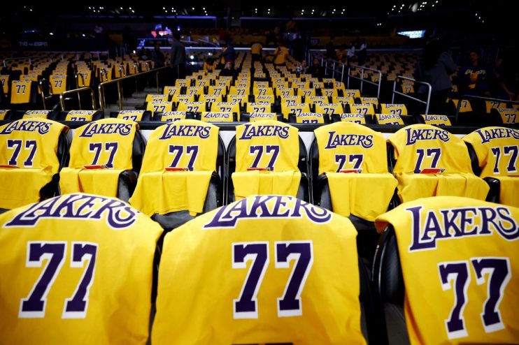 Rows of yellow Lakers jerseys with 77 on seats in a dark basketball arena.