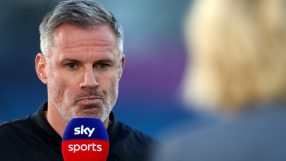 Jamie Carragher speaking into a Sky Sports microphone during an interview, with a blurred background.
