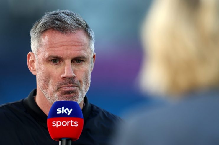 Jamie Carragher speaking into a Sky Sports microphone during an interview, with a blurred background.