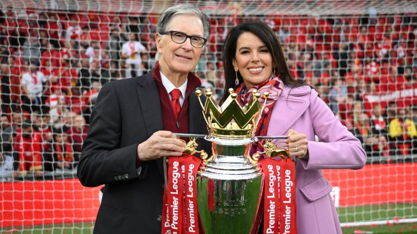 John W. Henry and Linda Pizzuti Henry with the Premier League trophy at a stadium.
