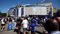 Crowds of fans gather outside the Chelsea FC stadium on a sunny day, with a Matchday Programmes On Sale sign visible.