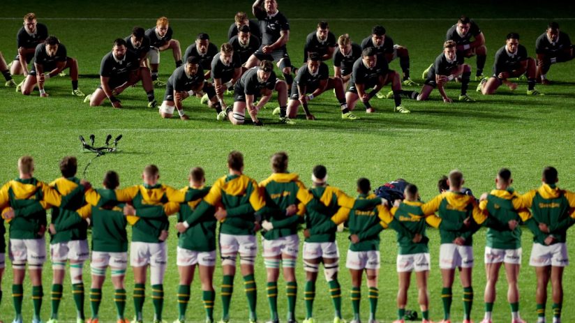 New Zealand All Blacks perform the Haka facing South African Springboks rugby team on field.