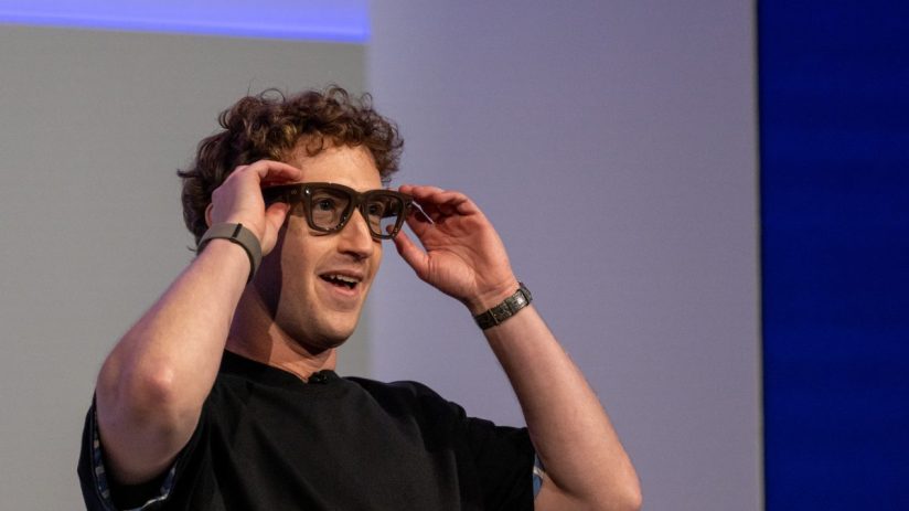 Mark Zuckerberg smiling while adjusting smart glasses on his face, wearing a black shirt and two wristbands