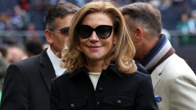 Smiling woman with blonde hair and black sunglasses in a black coat