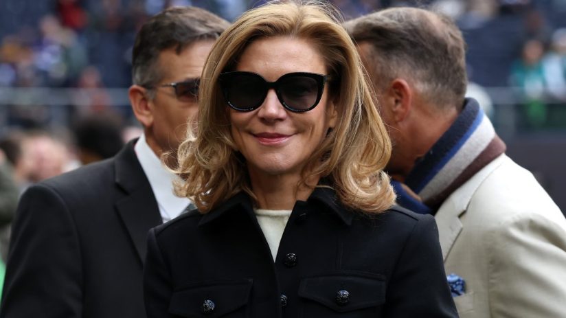 Smiling woman with blonde hair and black sunglasses in a black coat