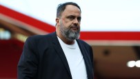 Evangelos Marinakis, owner of Nottingham Forest, in a dark jacket and white shirt, looking serious at a stadium.