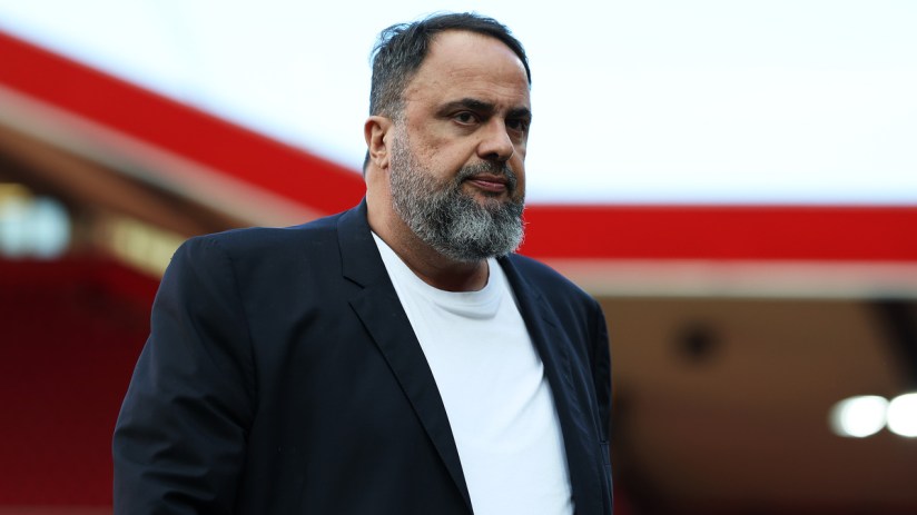 Evangelos Marinakis, owner of Nottingham Forest, in a dark jacket and white shirt, looking serious at a stadium.