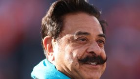 Shahid Khan, businessman, smiling and wearing a bright blue scarf, looking to the right with a blurred background.