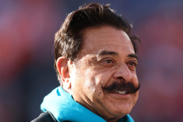 Shahid Khan, businessman, smiling and wearing a bright blue scarf, looking to the right with a blurred background.