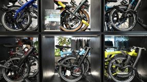 Six Brompton folding bicycles in various colors displayed in individual black cubbies.