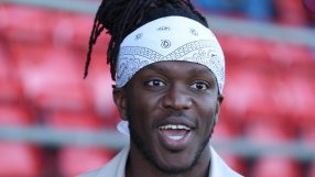 KSI with dreadlocks and a white bandana, smiling with an open mouth, red stadium seats blurred in background.