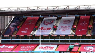 Empty stadium stands with large banners supporting MND awareness, Gloucester Rugby, and the Slater Cup.