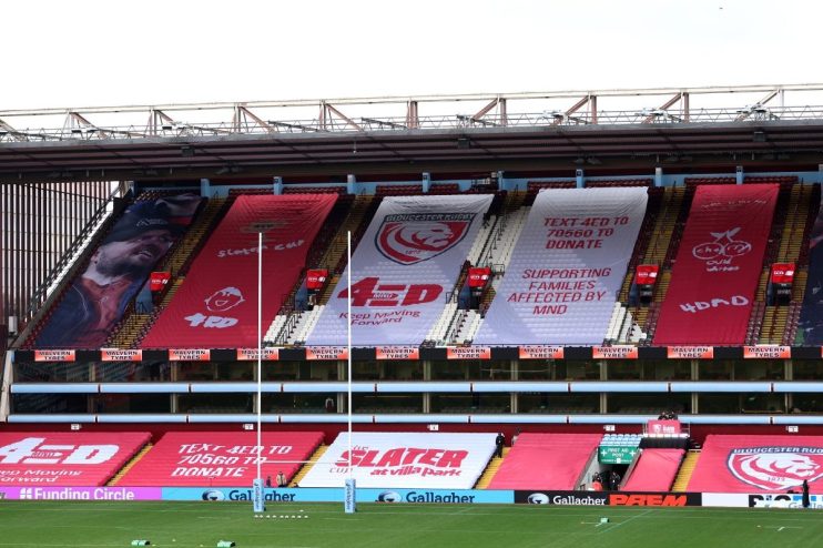Empty stadium stands with large banners supporting MND awareness, Gloucester Rugby, and the Slater Cup.