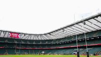 Rugby stadium interior with large screen displaying Red Roses v Ireland, goalposts, and empty green seats