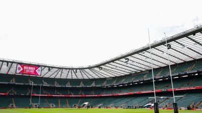 Rugby stadium interior with large screen displaying Red Roses v Ireland, goalposts, and empty green seats