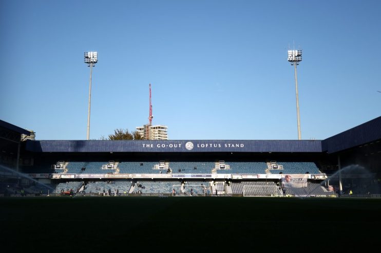 Loftus Road stadium with THE GO-OUT LOFTUS STAND sign, floodlights, and sprinklers on the pitch.