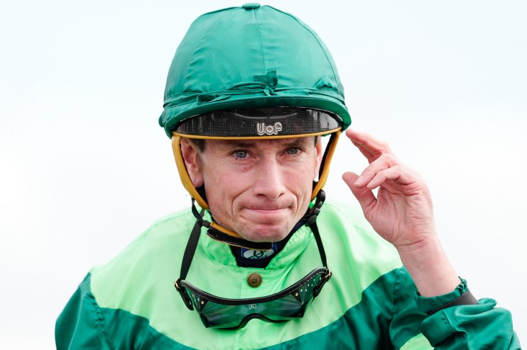 Jockey in green and light green silks, wearing a helmet and goggles, adjusting his headwear.