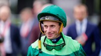 Jockey in green and dark green silks, wearing a green helmet, smiling with goggles around his neck