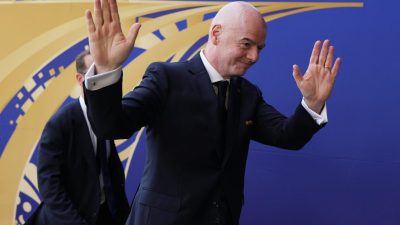 Gianni Infantino, FIFA President, waves to a crowd with a blue and gold patterned background