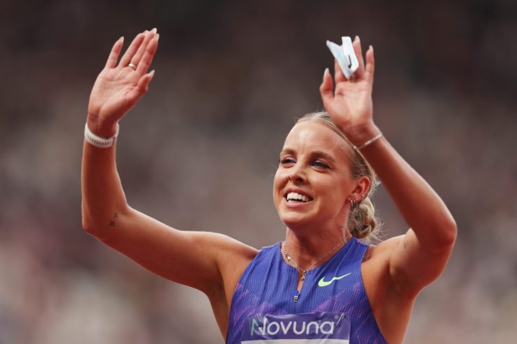 Keely Hodgkinson waves to the crowd at a track and field event, wearing a purple and black athletic top.